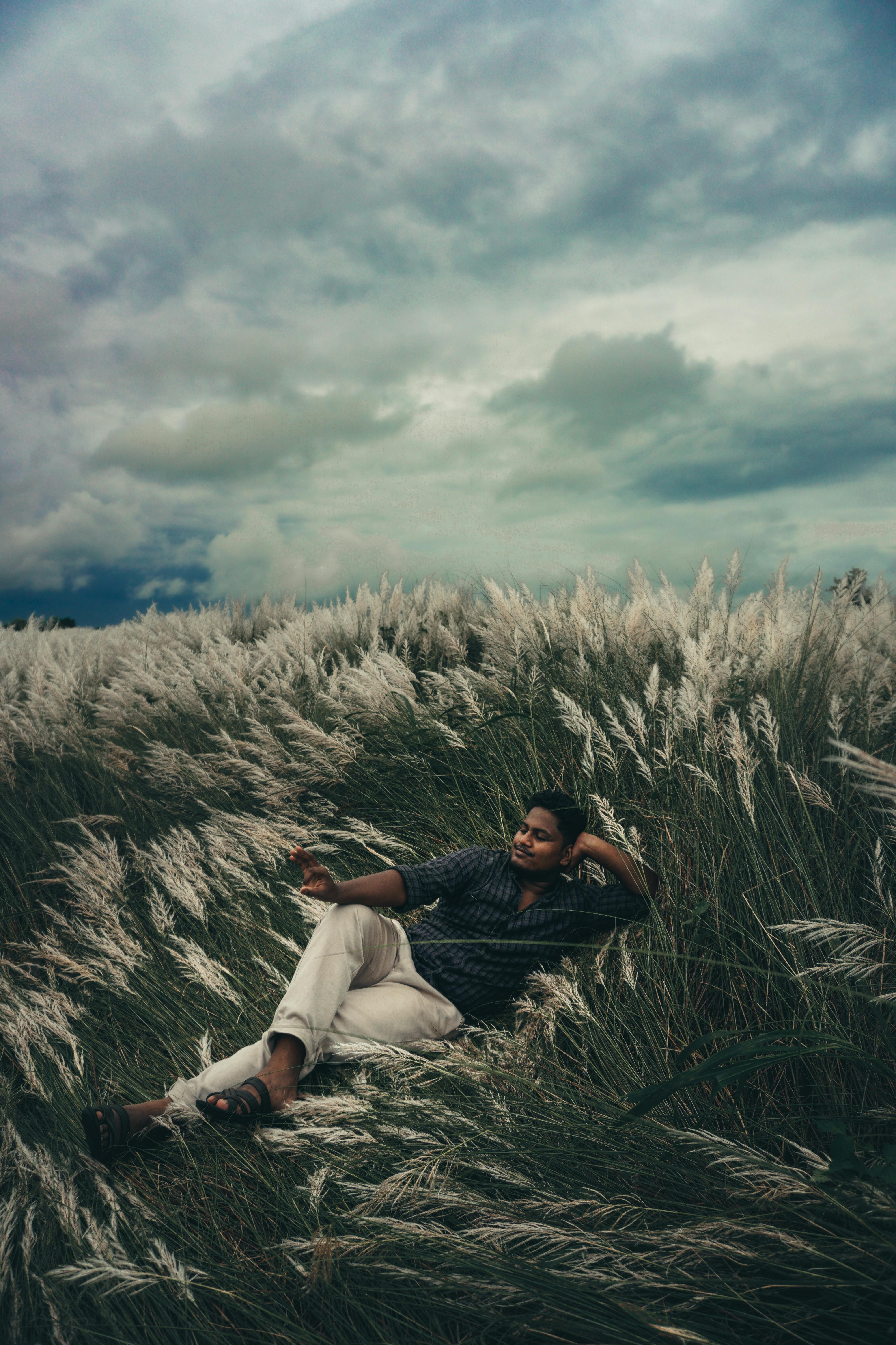A person lounges in a lush grassy meadow, with ominous storm clouds rolling above, depicting tranquility before a storm.