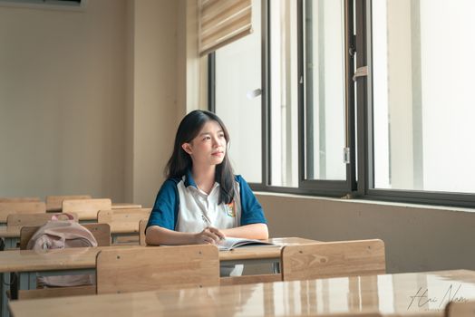 A student sits alone in a classroom, gazing out the window, contemplating. Bright natural light fills the room.