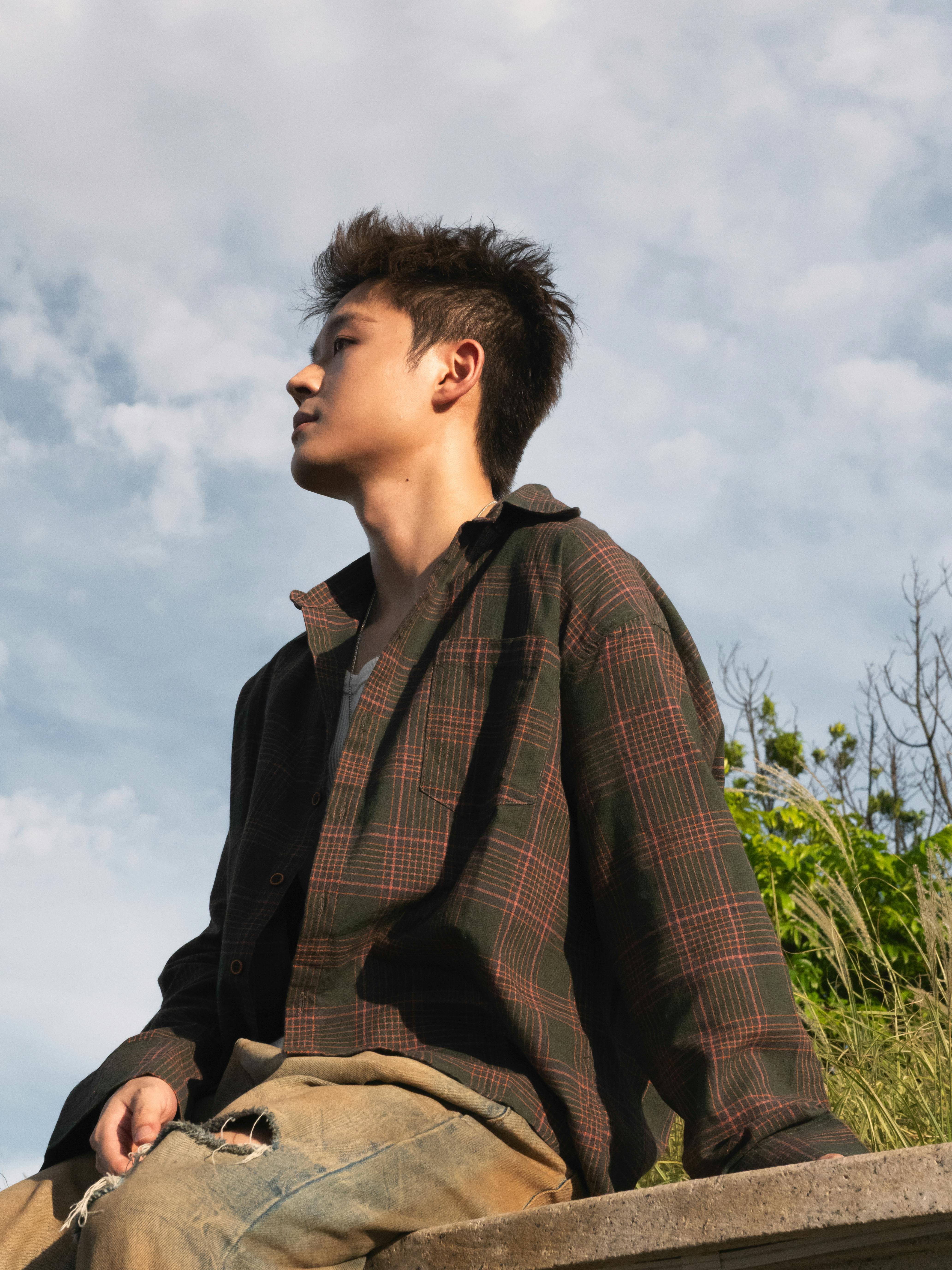 ingyenes Kockás inges fiatalember ül a szabadban, élvezi a napsütéses napot. Stockfotó