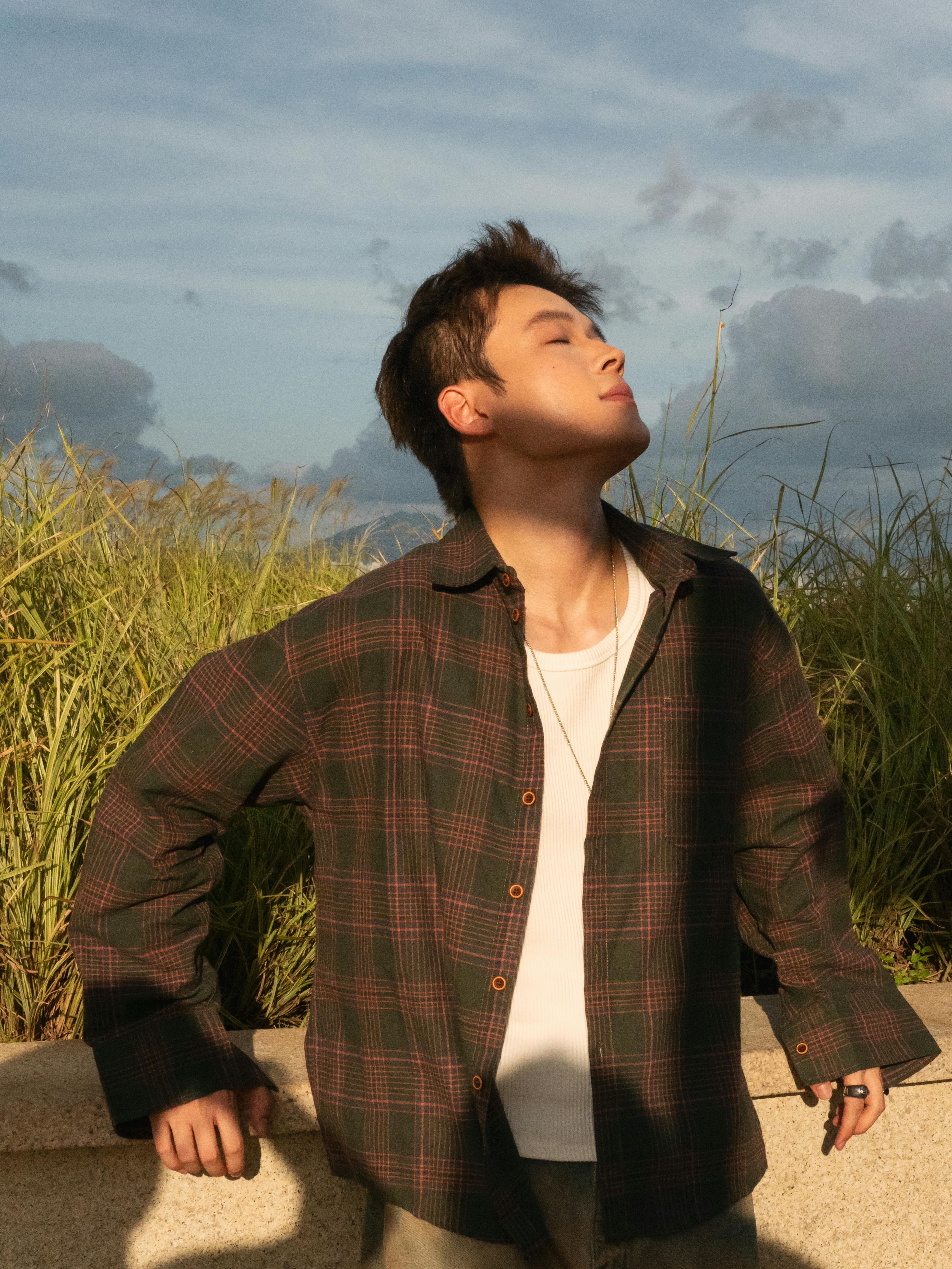 免费 一名年轻的成年男子闭着眼睛，在户外草地上欣赏宁静的日落。 素材图片