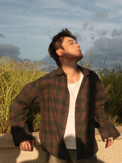 Free A young adult male, with eyes closed, enjoying a serene sunset in a grassy outdoor setting. Stock Photo