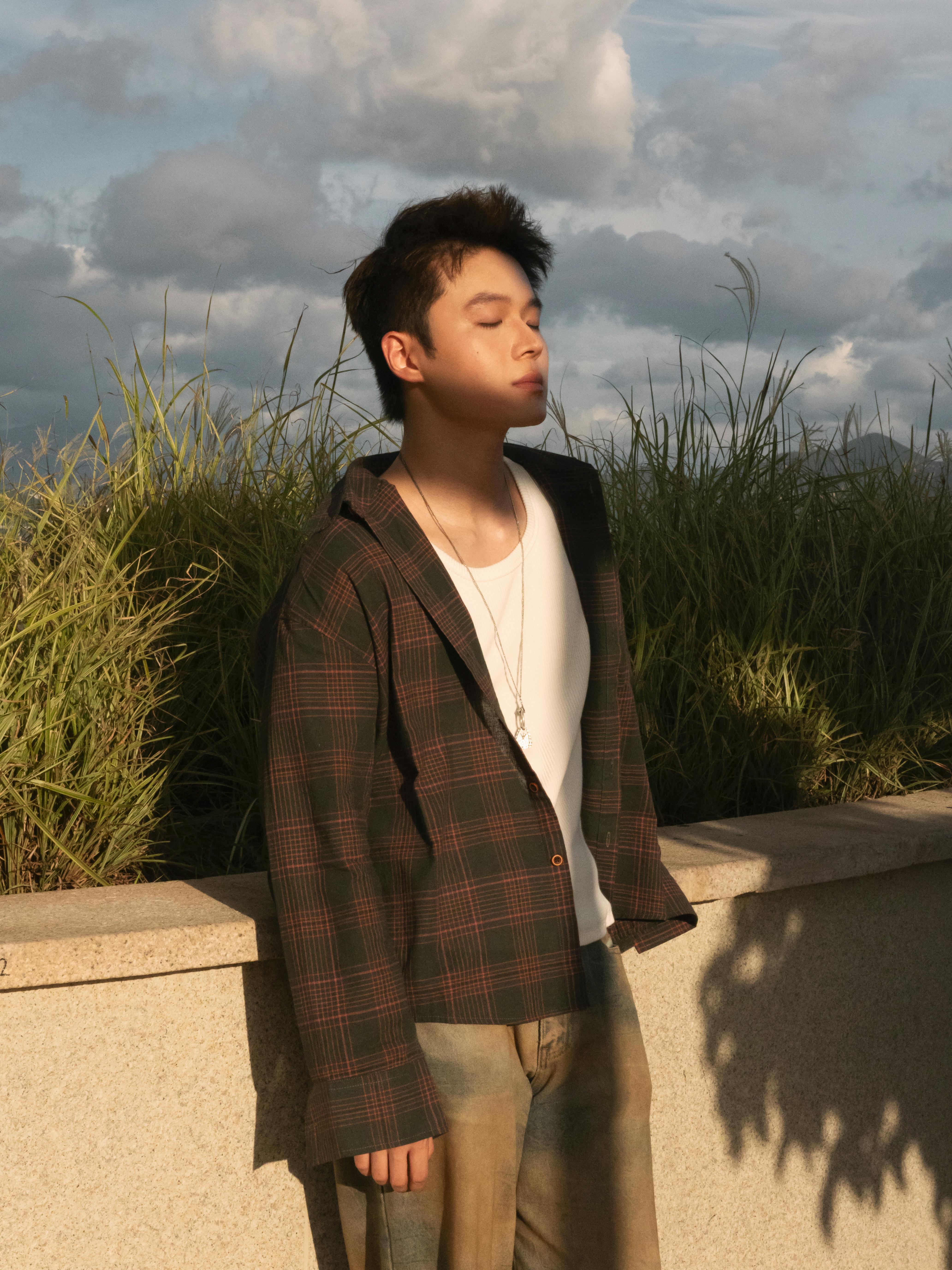 Gratuit Un jeune homme en tenue décontractée se prélasse dans la chaude lumière du soleil, embrassant la tranquillité. Photos