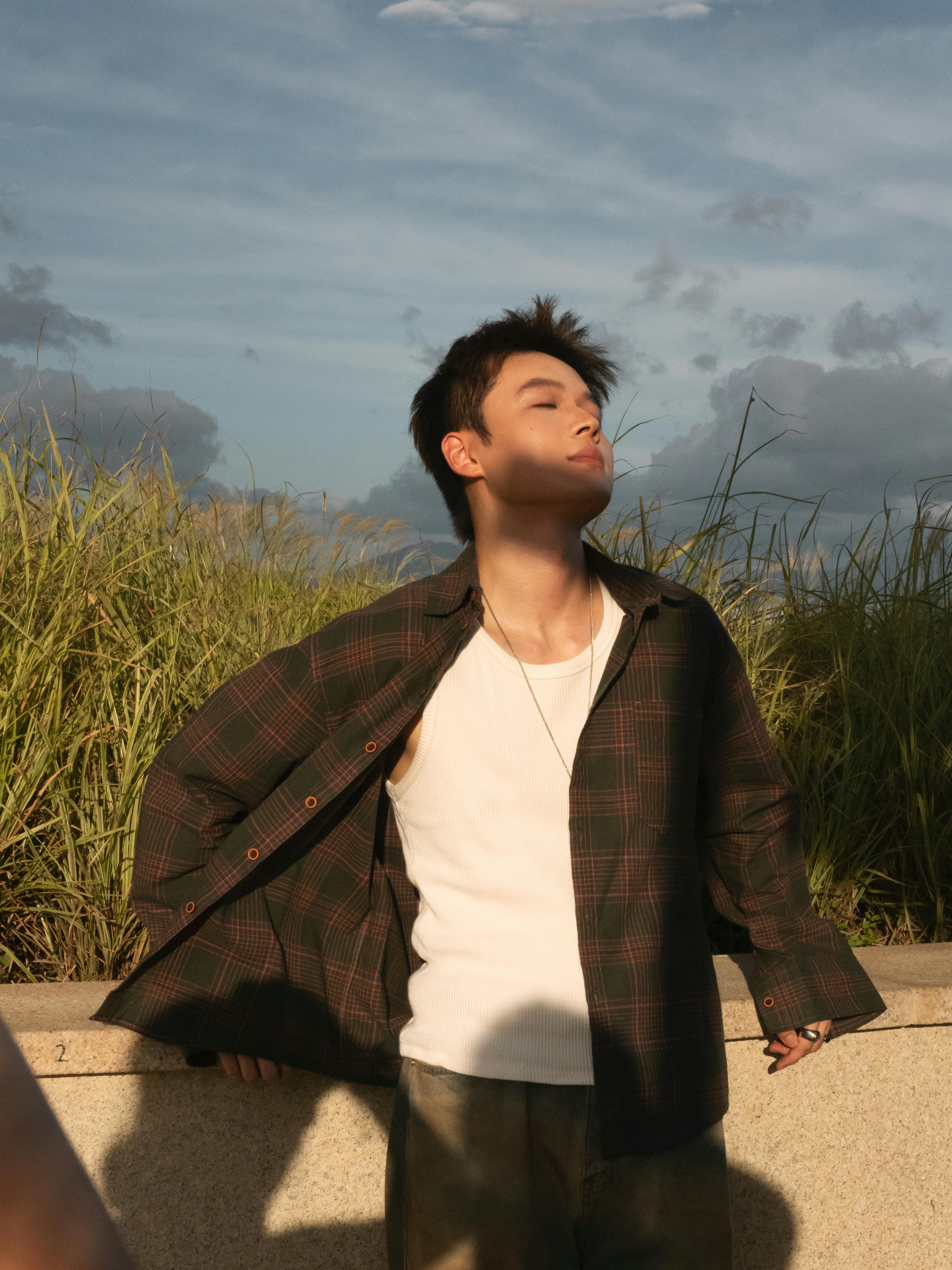 Gratis En ung mann nyter solnedgangen med lukkede øyne, og nyter det gylne lyset utendørs. Arkivbilde