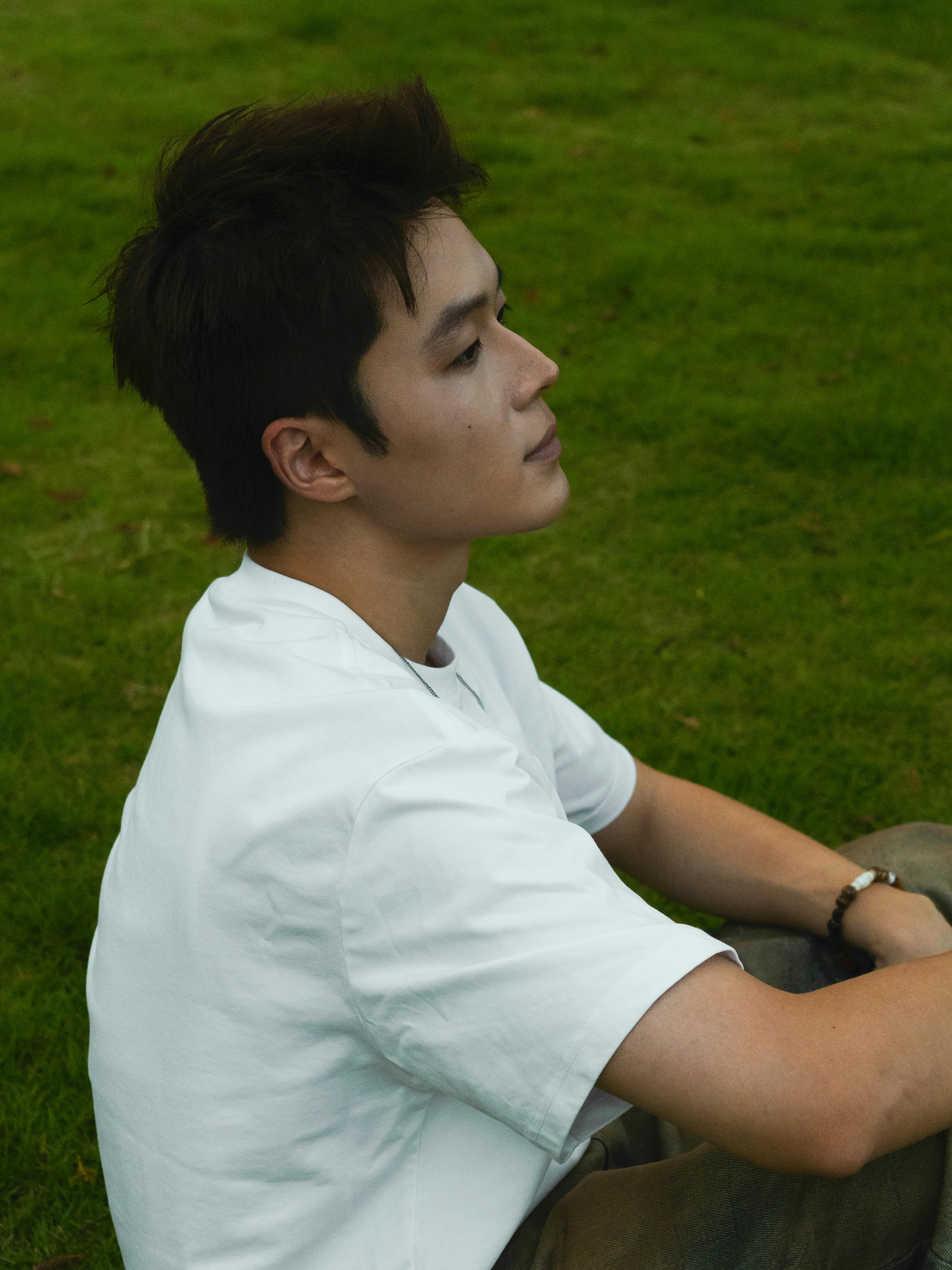 免费 一位年轻人的侧面坐在绿草地上，在户外陷入沉思。 素材图片