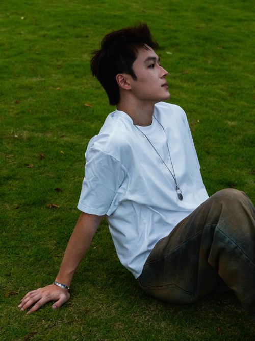 Free A young adult casually sitting on a grassy field, exuding a relaxed and contemplative mood. Stock Photo