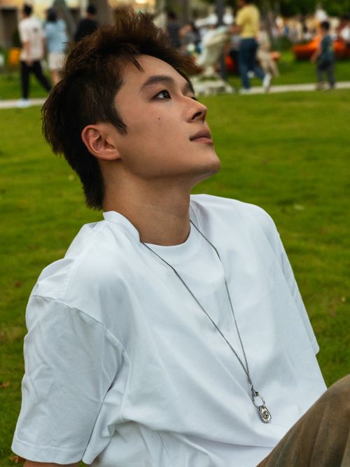 Free A young man in a white shirt relaxes on the grass in a park on a sunny day. Stock Photo