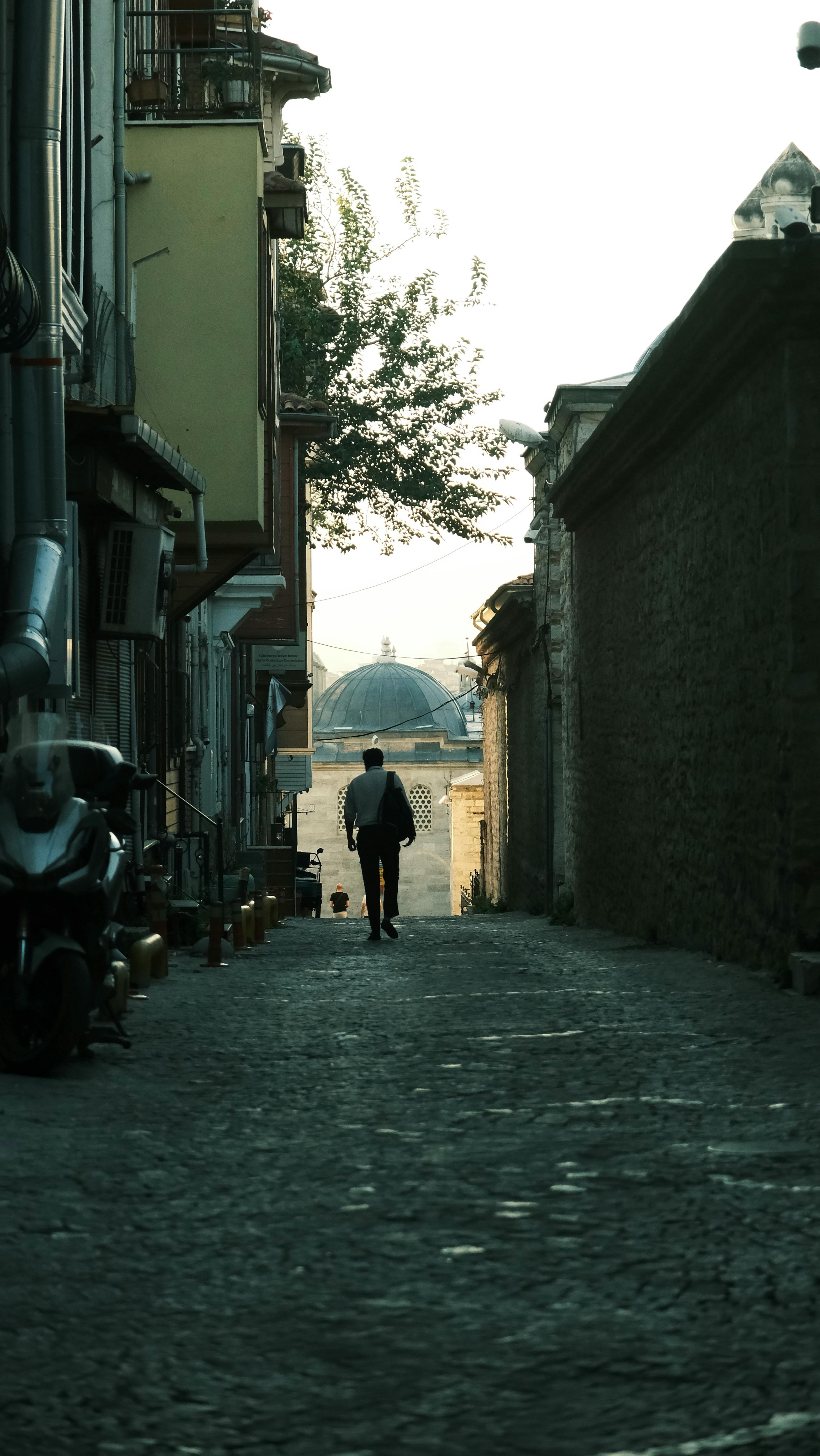 A lone person walking through a historic alley at twilight in a quiet, ancient city.