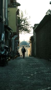 A lone person walking through a historic alley at twilight in a quiet, ancient city.