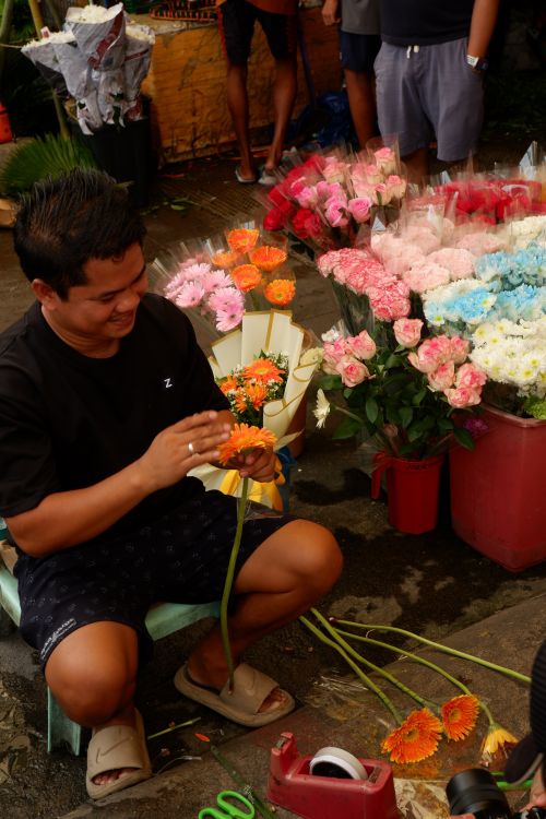 Free A florist joyfully arranges colorful flowers at an outdoor market. Stock Photo