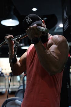 Muscular man doing bicep curls in a modern gym wearing a cap and tank top.