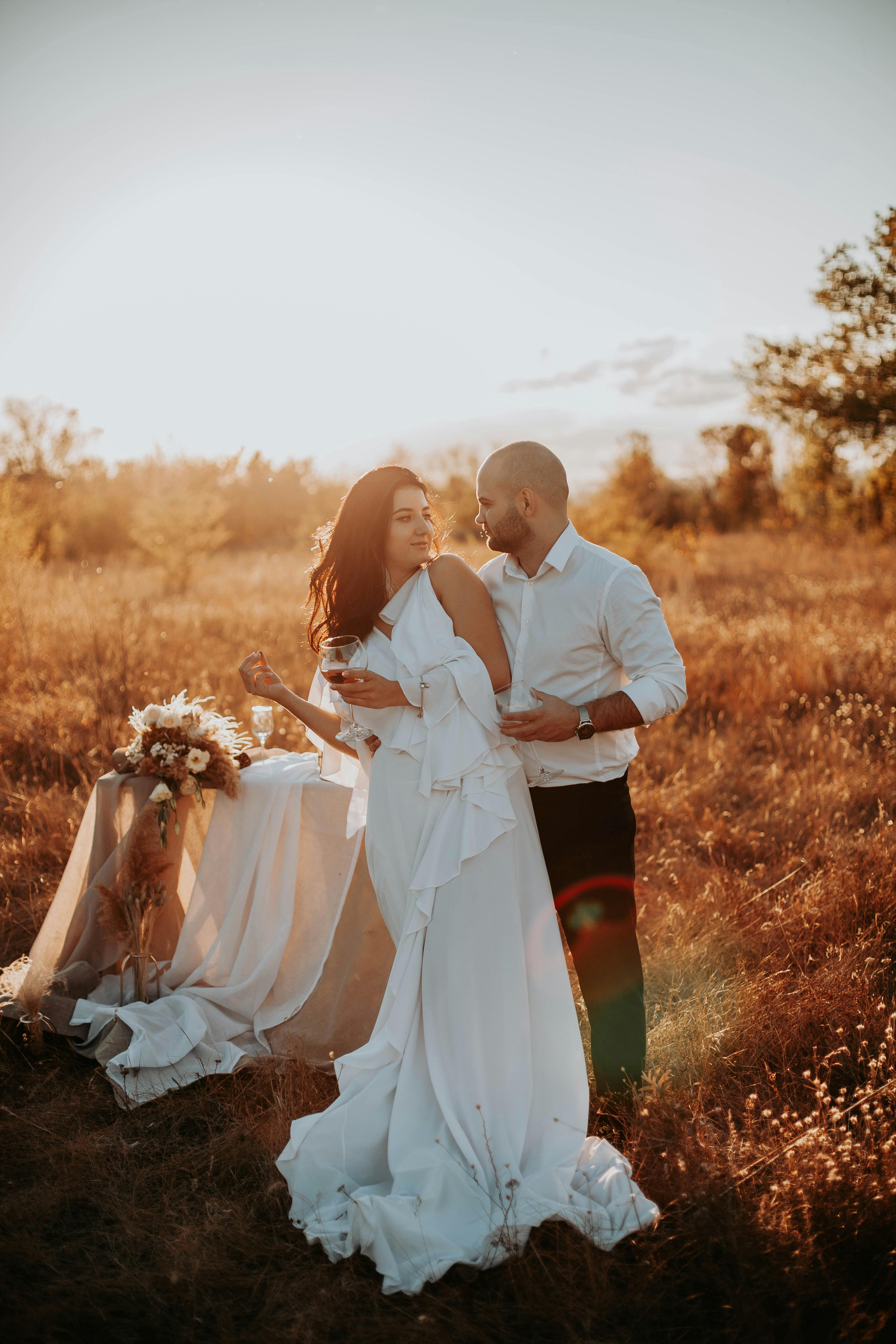 免費 新娘和新郎在陽光明媚的田野中擁抱，捕捉浪漫的戶外婚禮時刻。 圖庫相片