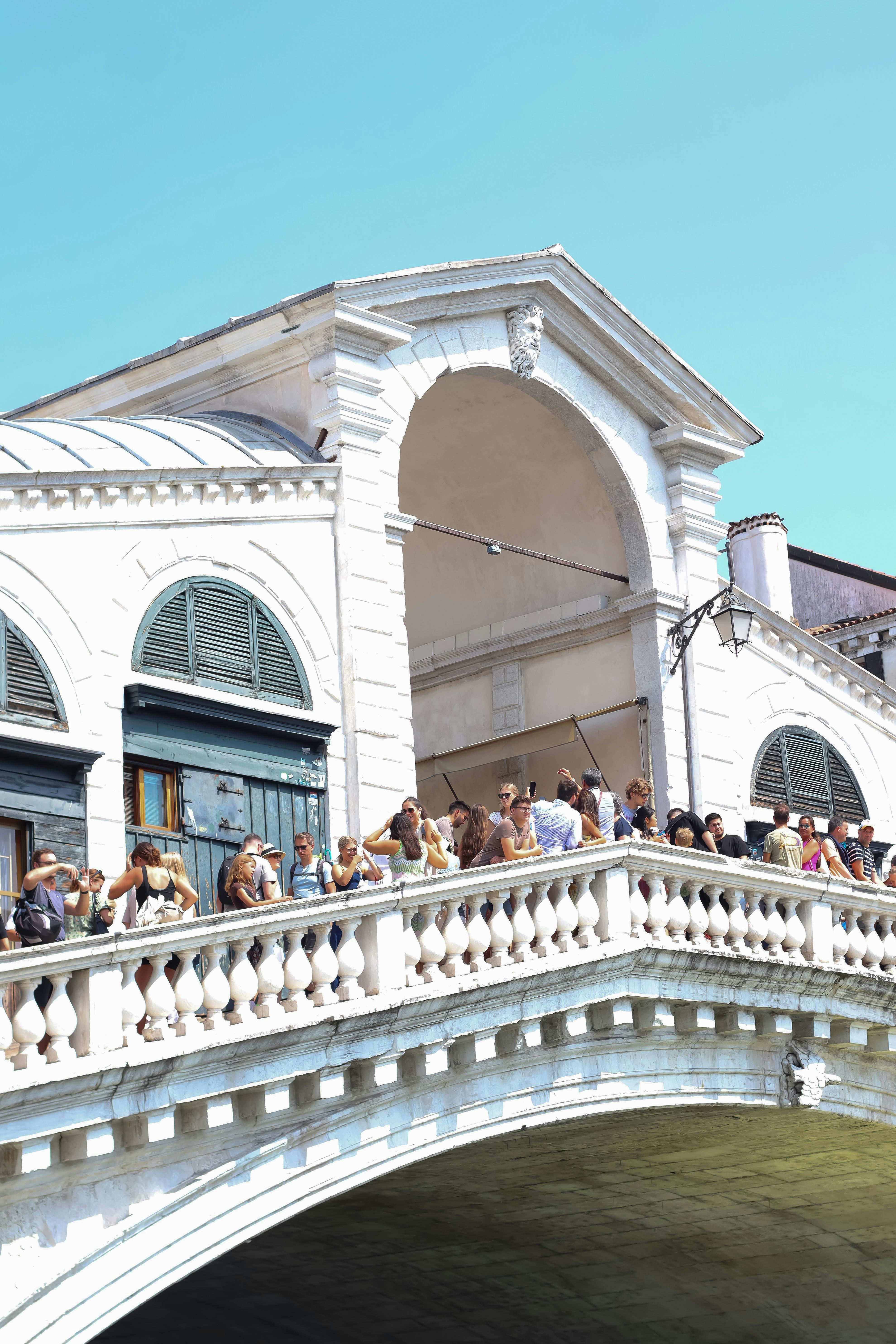 Sunny day at the iconic Rialto Bridge in Venice, bustling with tourists.