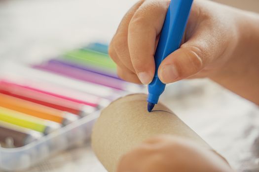 A close-up view of a child using colorful markers and a paper tube for creative drawing.