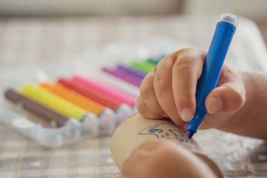 A child using a blue marker to draw on paper, surrounded by colorful markers. Creativity and art.