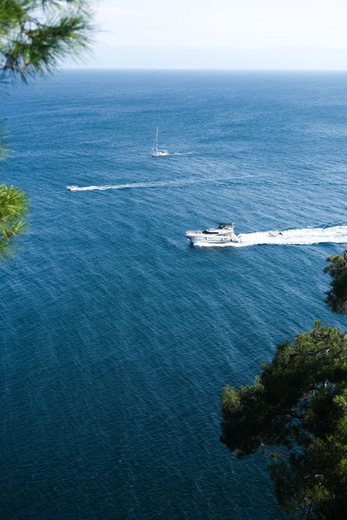 Free Aerial view of boats cruising on the open sea, framed by evergreen trees. Stock Photo