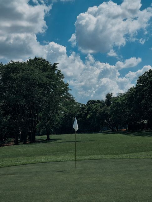 Photo by Chimango Hara Tranquil golf course with trees and a flag under a blue sky with clouds.
