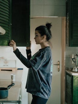 A young woman looks inside a kitchen cabinet. Soft lighting creates a warm, homey atmosphere.