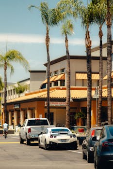 A Nissan GTR parked in a bustling Californian street lined with palm trees and vibrant buildings.