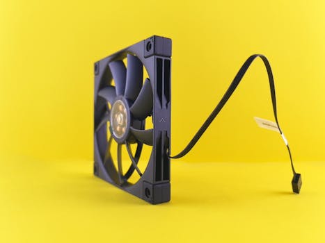 Black computer cooling fan with cable against vibrant yellow background, side view.
