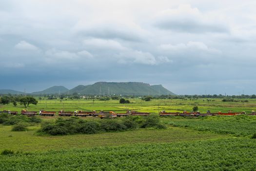 Scenic view of a train passing through lush green fields with mountains in the background.