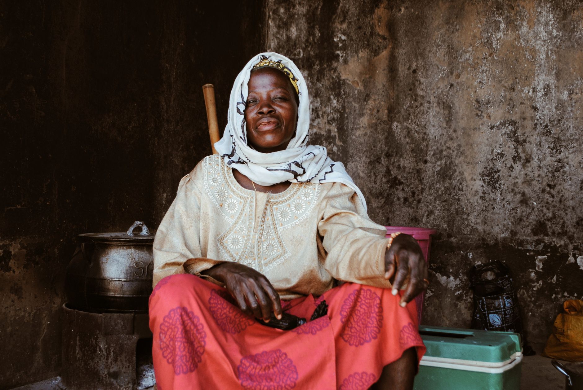 Portrait of an African woman wearing traditional clothing, seated indoors against a rustic wall.