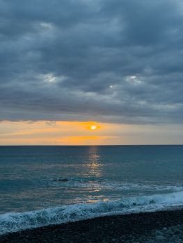 Tranquil ocean sunset casting warm reflections over a pebble beach.