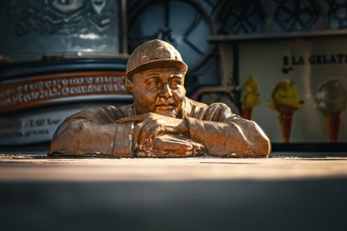 Free Bronze statue of a man thoughtfully leaning on a ledge, captured in warm sunlight. Stock Photo