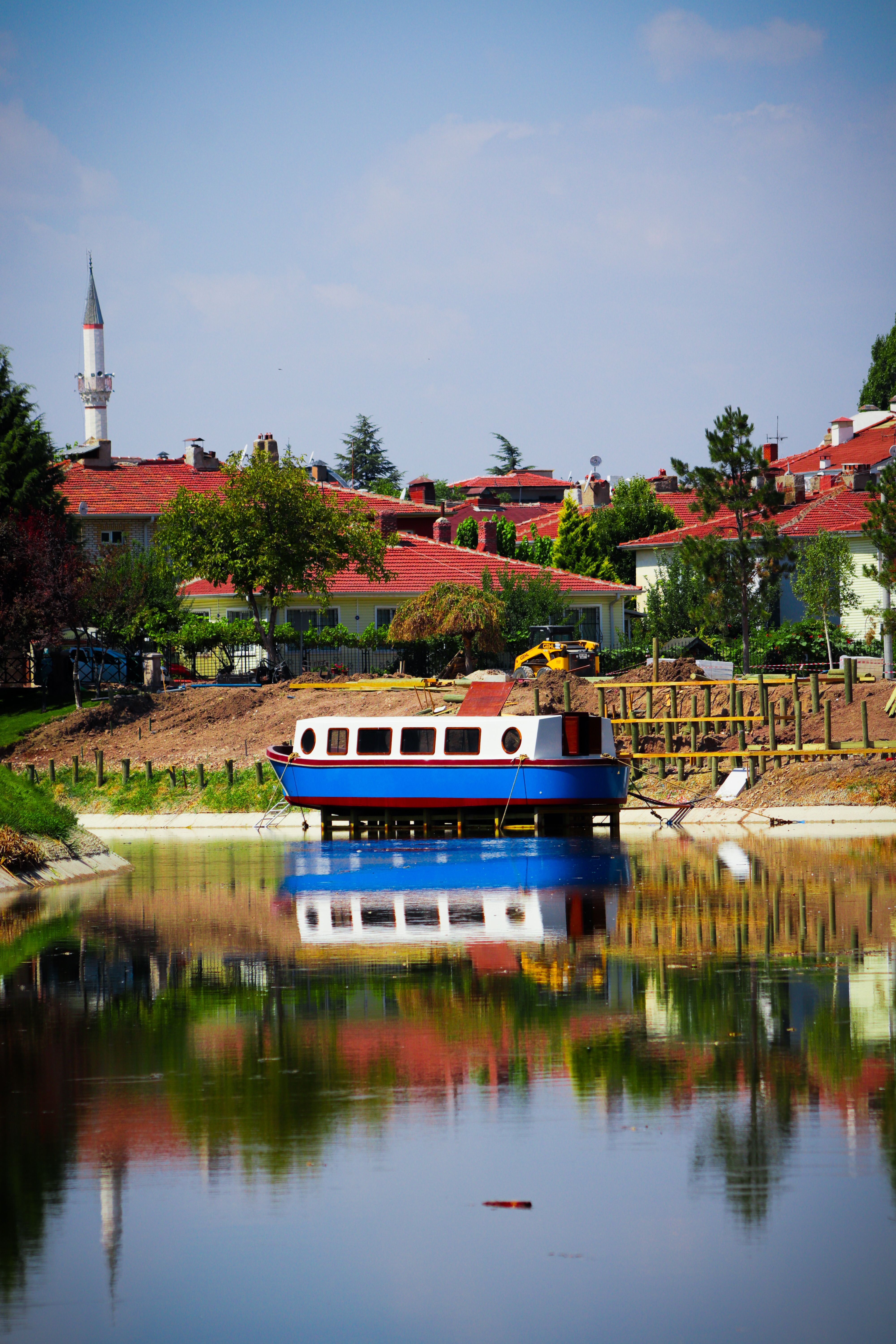 A picturesque riverboat moored with reflections near a quaint town under a clear blue sky.