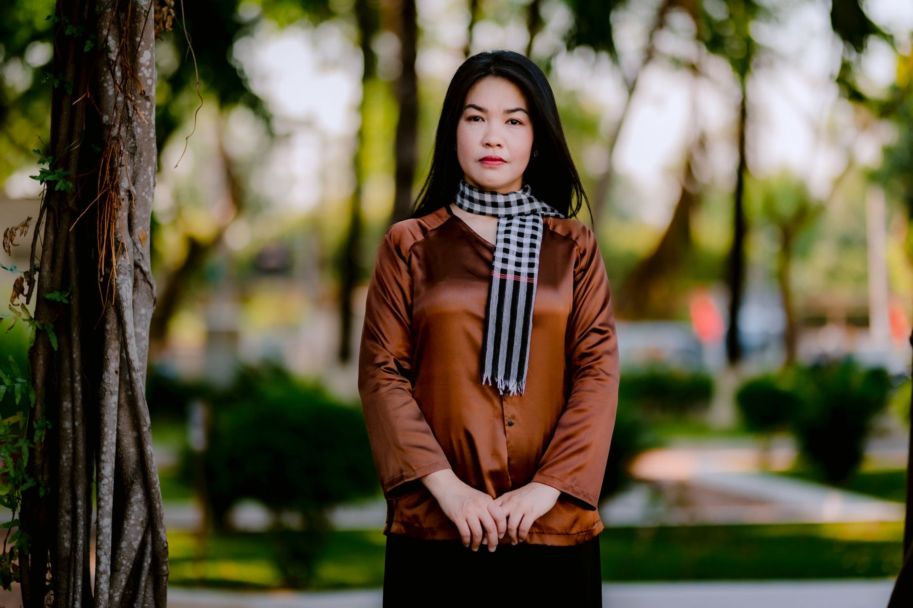 Confident woman in silk blouse and scarf posing gracefully outdoors in a green park.