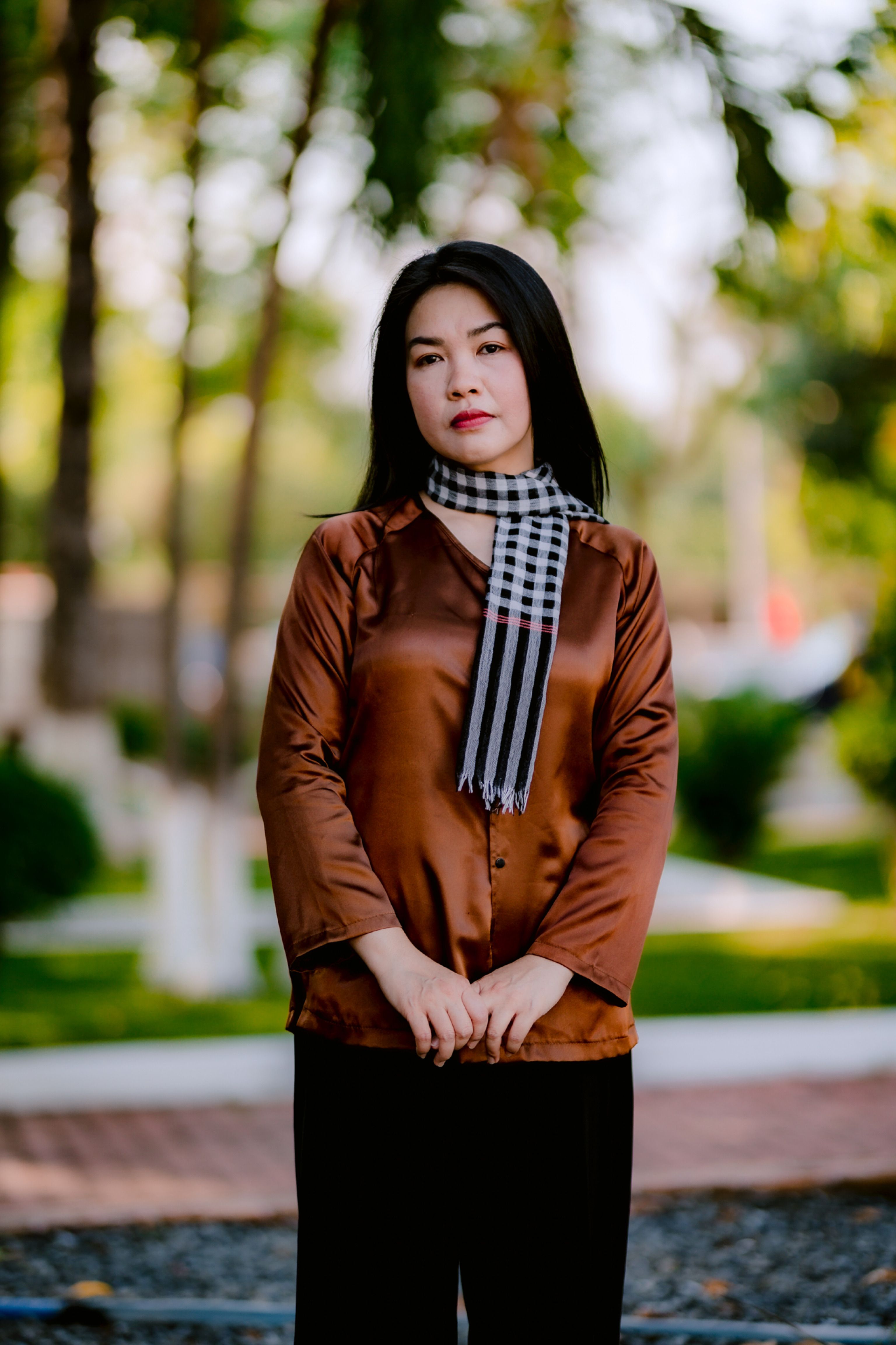 Stylish woman in brown top and plaid scarf enjoying a serene outdoor setting.