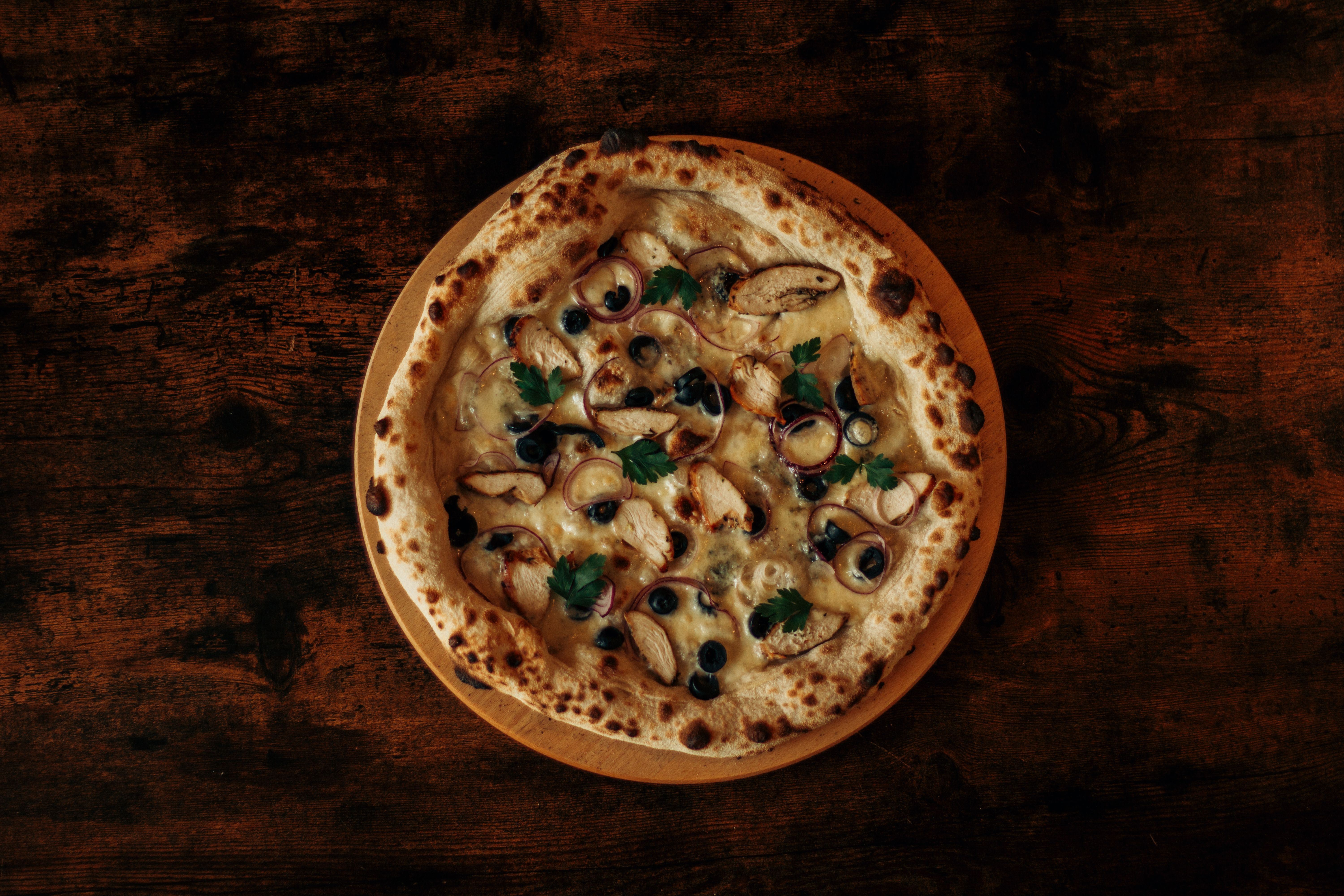 Mouthwatering artisan pizza topped with olives, chicken, and parsley on a rustic table. Mouthwatering artisan pizza topped with olives, chicken, and parsley on a rustic table.