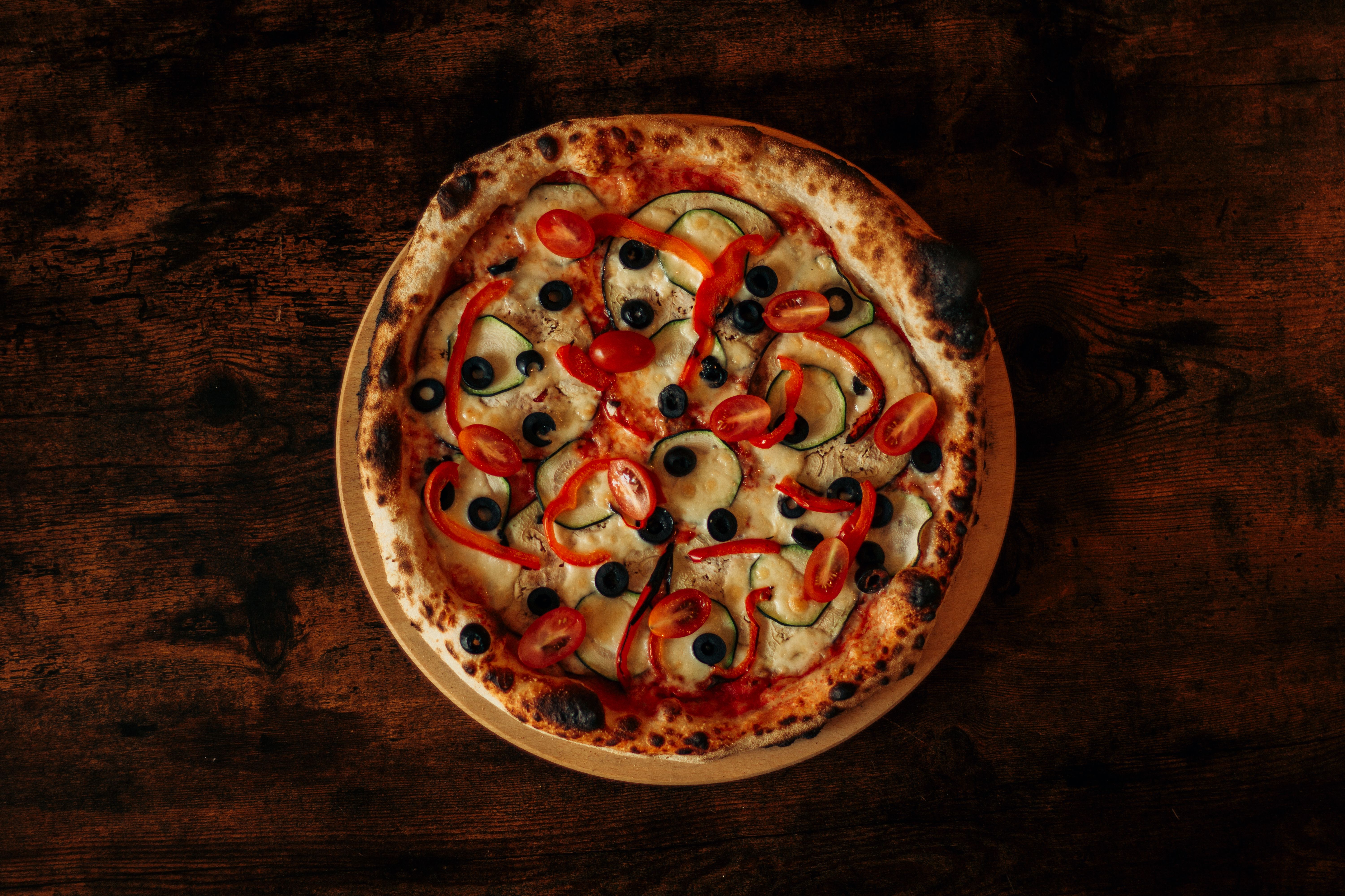 Ilmainen Ylhäältä päin tuoreista kasviksista valmistettua pizzaa oliiveilla ja paprikoilla puupöydällä. Kuvapankkikuva