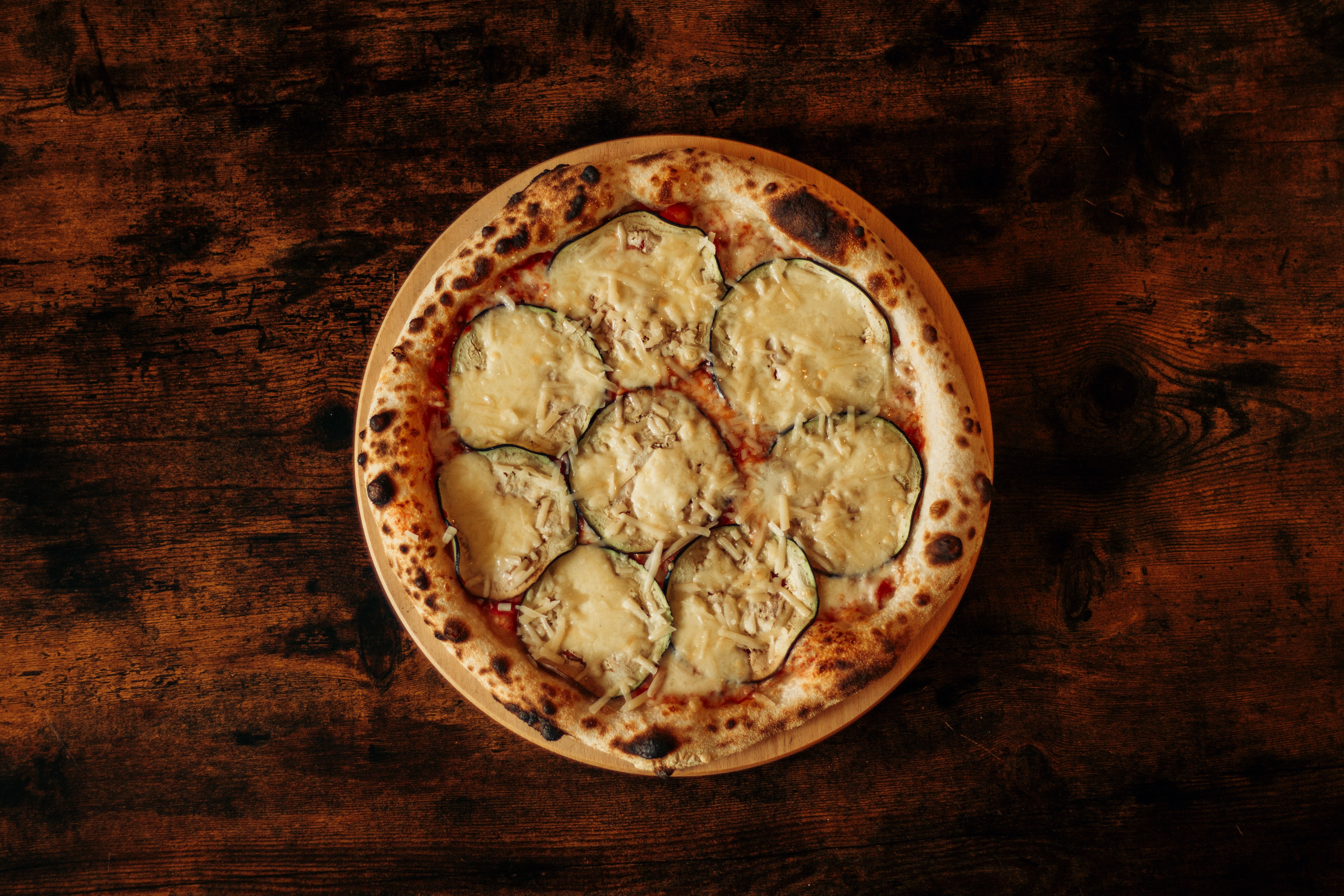 Tasty eggplant pizza with cheese on a rustic wooden table, perfect for a cozy meal setting.