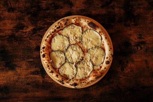 Tasty eggplant pizza with cheese on a rustic wooden table, perfect for a cozy meal setting.