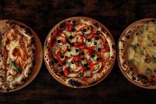 Three gourmet wood-fired pizzas with diverse toppings on a wooden table, showcasing Italian culinary craftsmanship.