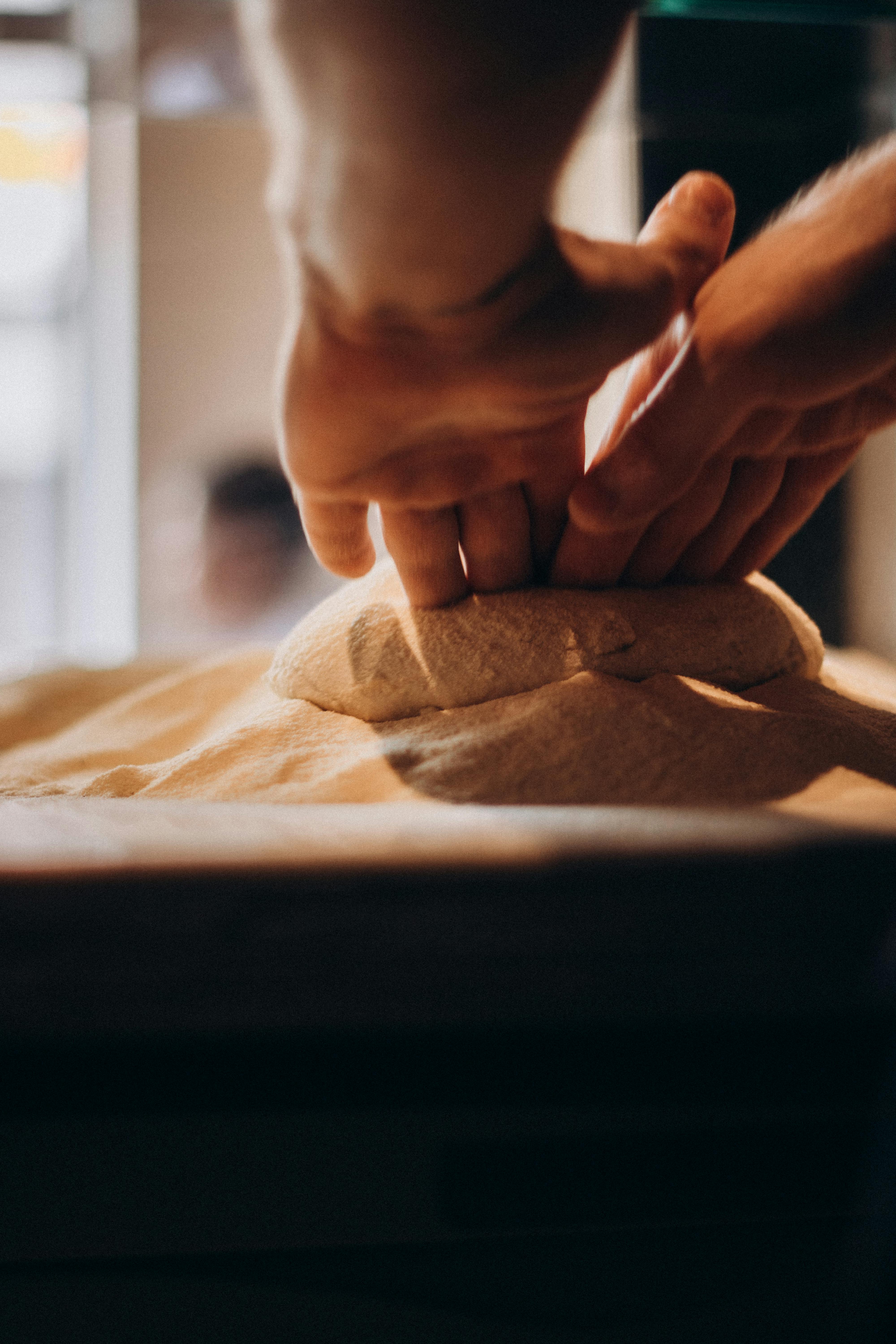 Mani che impastano energicamente su una superficie spolverata di farina fresca