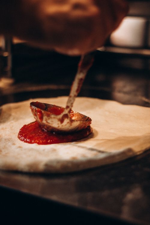 Free Chef spreading tomato sauce on pizza dough, showcasing traditional pizza making. Stock Photo