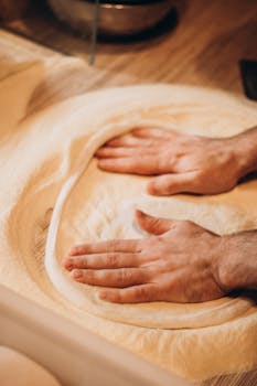 Hands shaping dough on a floured surface for homemade pizza preparation.