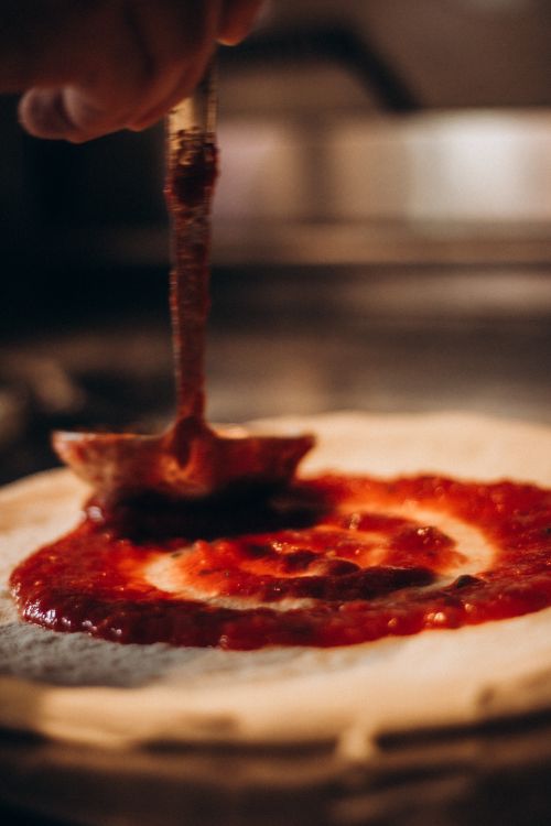 Free Chef adding tomato sauce to pizza dough for traditional Italian recipe. Stock Photo
