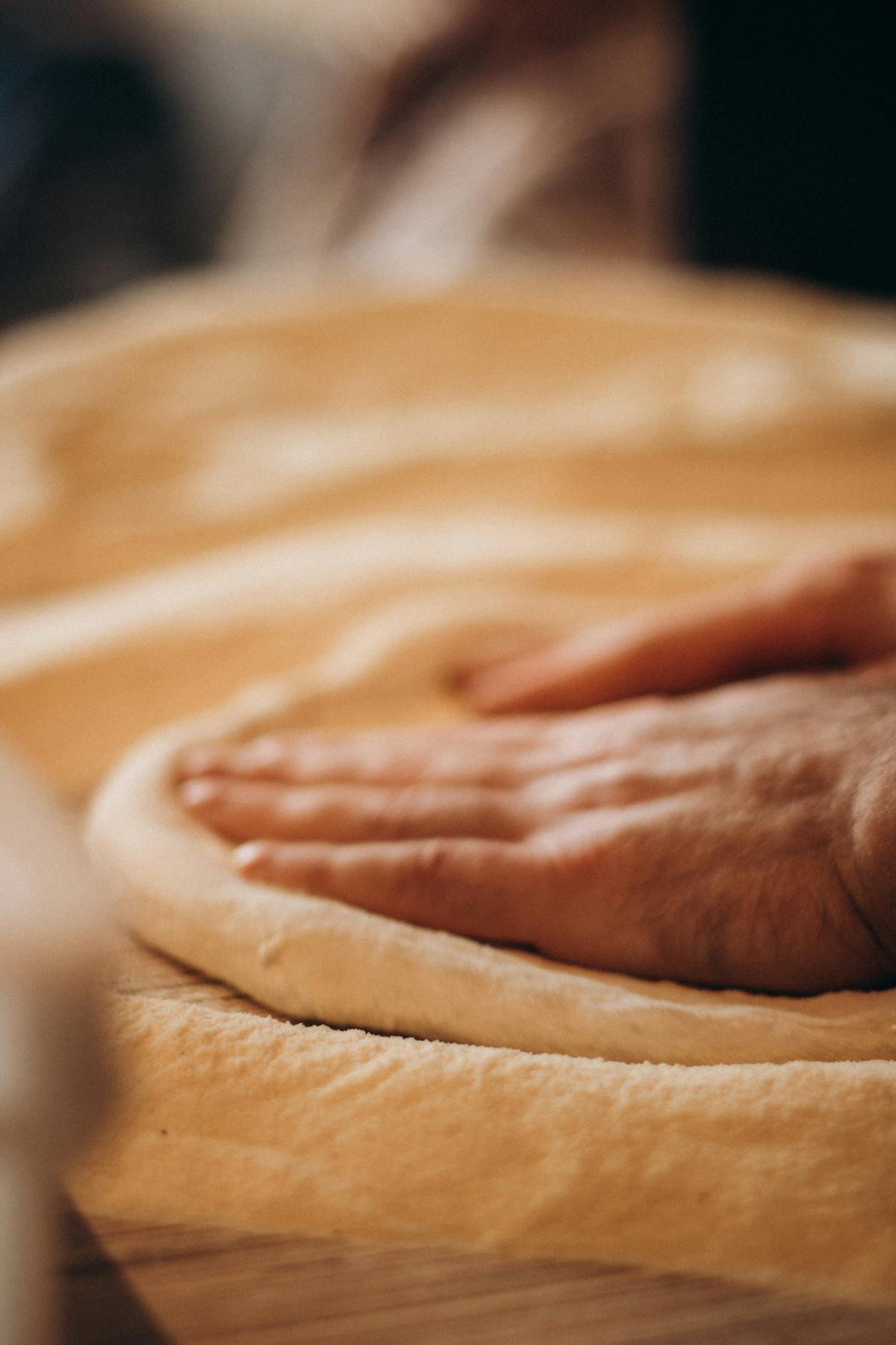 Mano che preme impasto morbido su superficie da pane