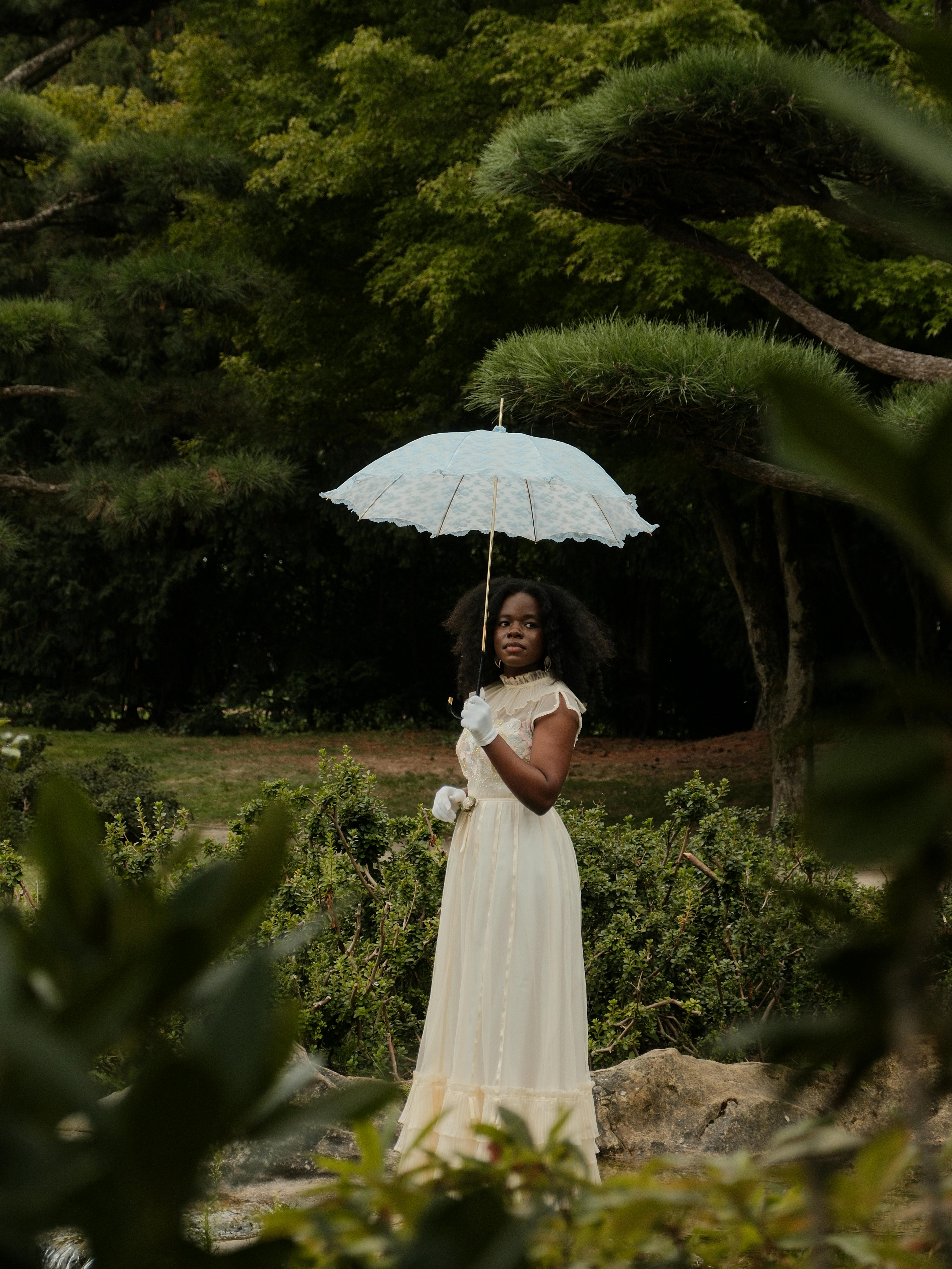 A woman in a vintage dress holding a parasol in a lush garden, evoking a classic, romantic atmosphere.
