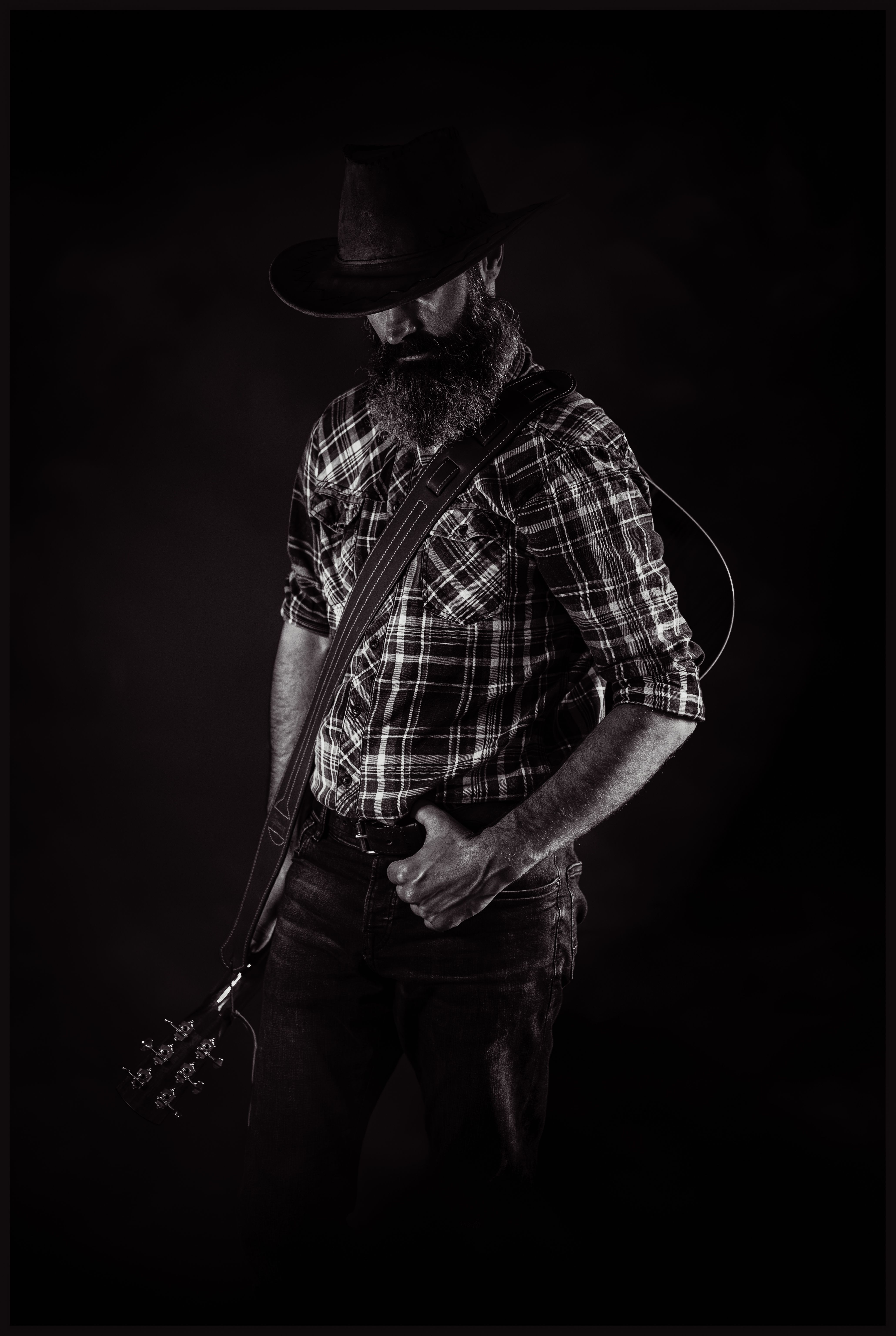 Dark and dramatic portrait of a cowboy with a guitar, exuding rugged charm.