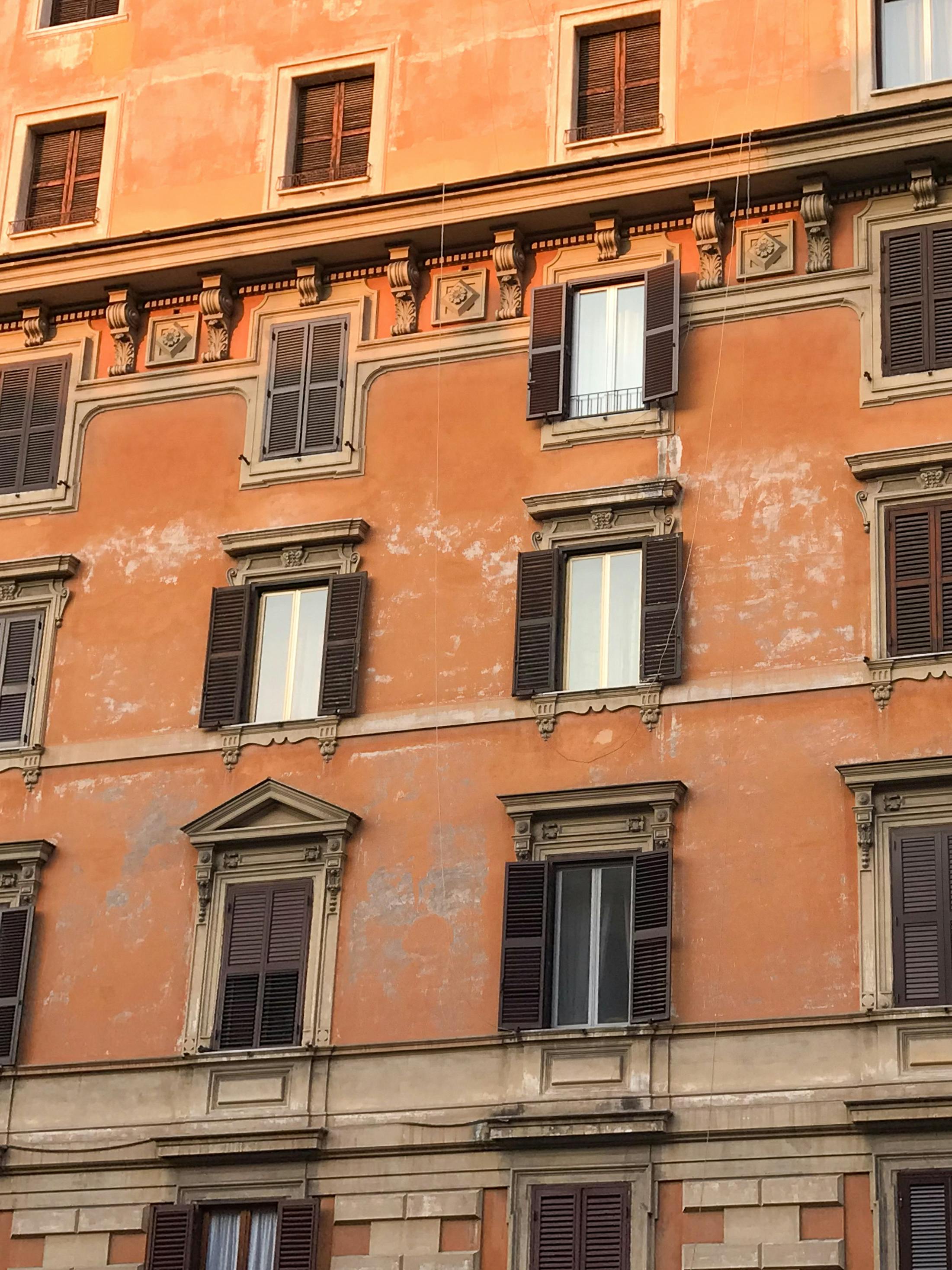 Orange facade of an Italian building with classic shutters, in Rome, Lazio, Italy.