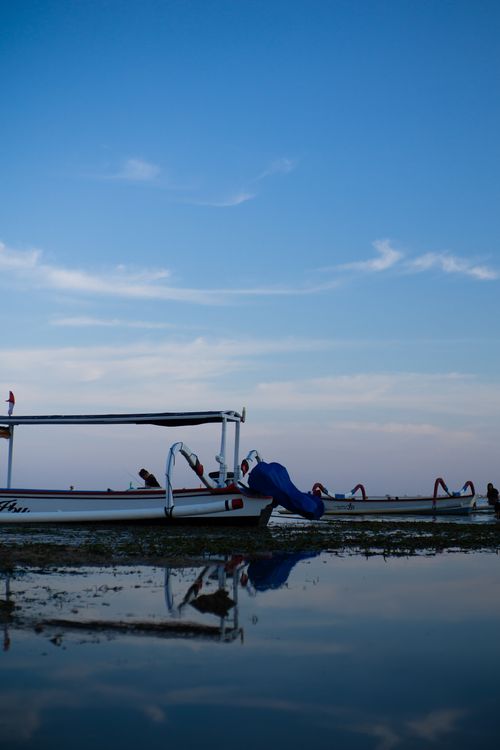 Free Serene view of traditional Indonesian fishing boats reflected in calm waters at sunrise in Bali. Stock Photo