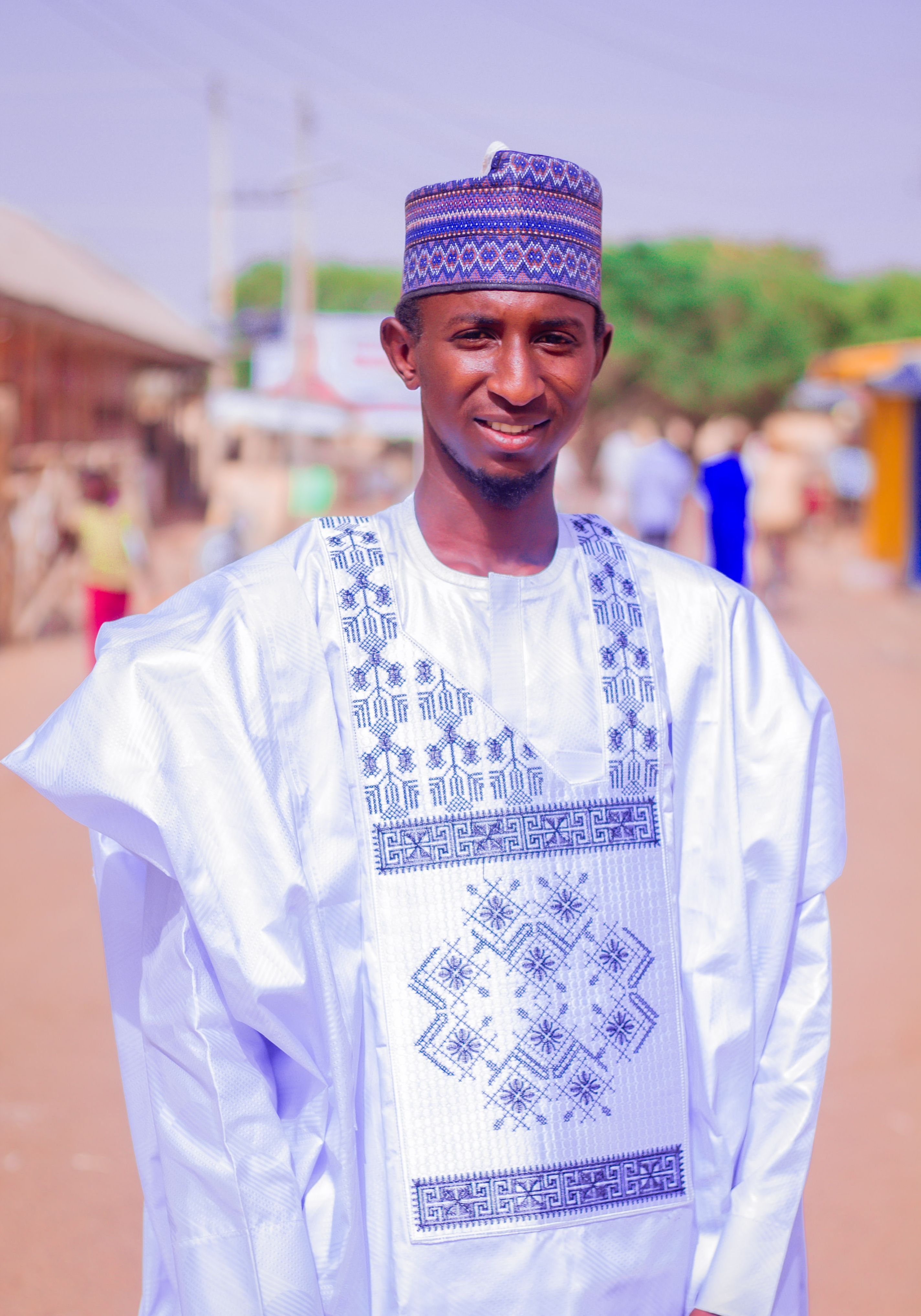 Smiling man wearing traditional African attire outdoors on a sunny day.