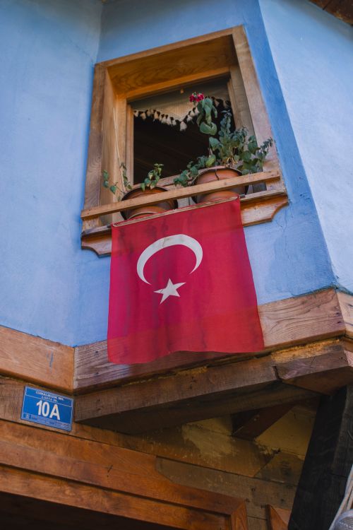 Free A Turkish flag hangs from a vibrant traditional window in Bursa, Türkiye. Stock Photo