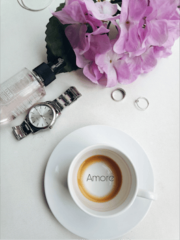 Stylish flat lay featuring coffee, pink flowers, a watch, and rings.