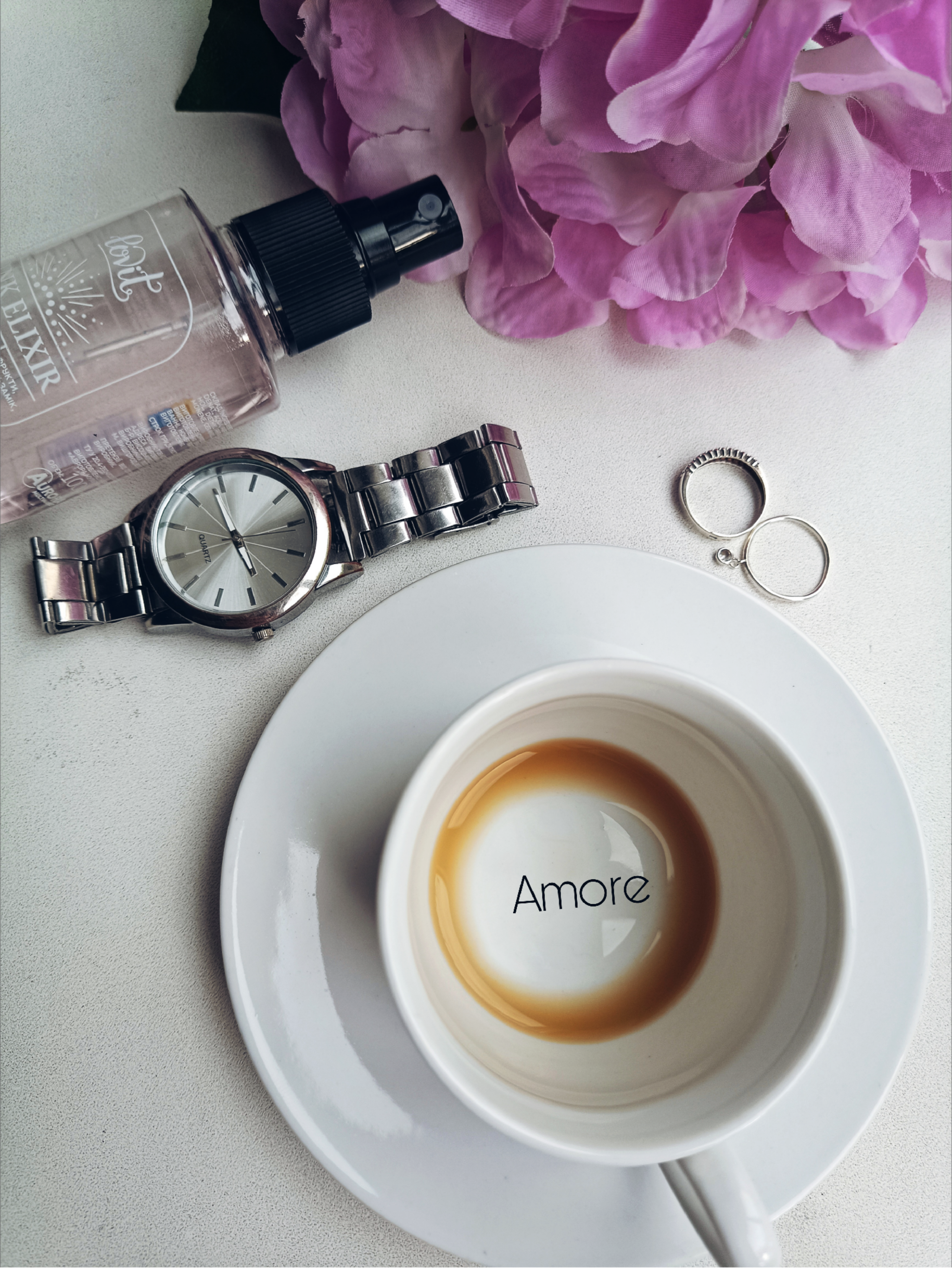 Chic flat lay with coffee cup, watch, rings, and flowers.