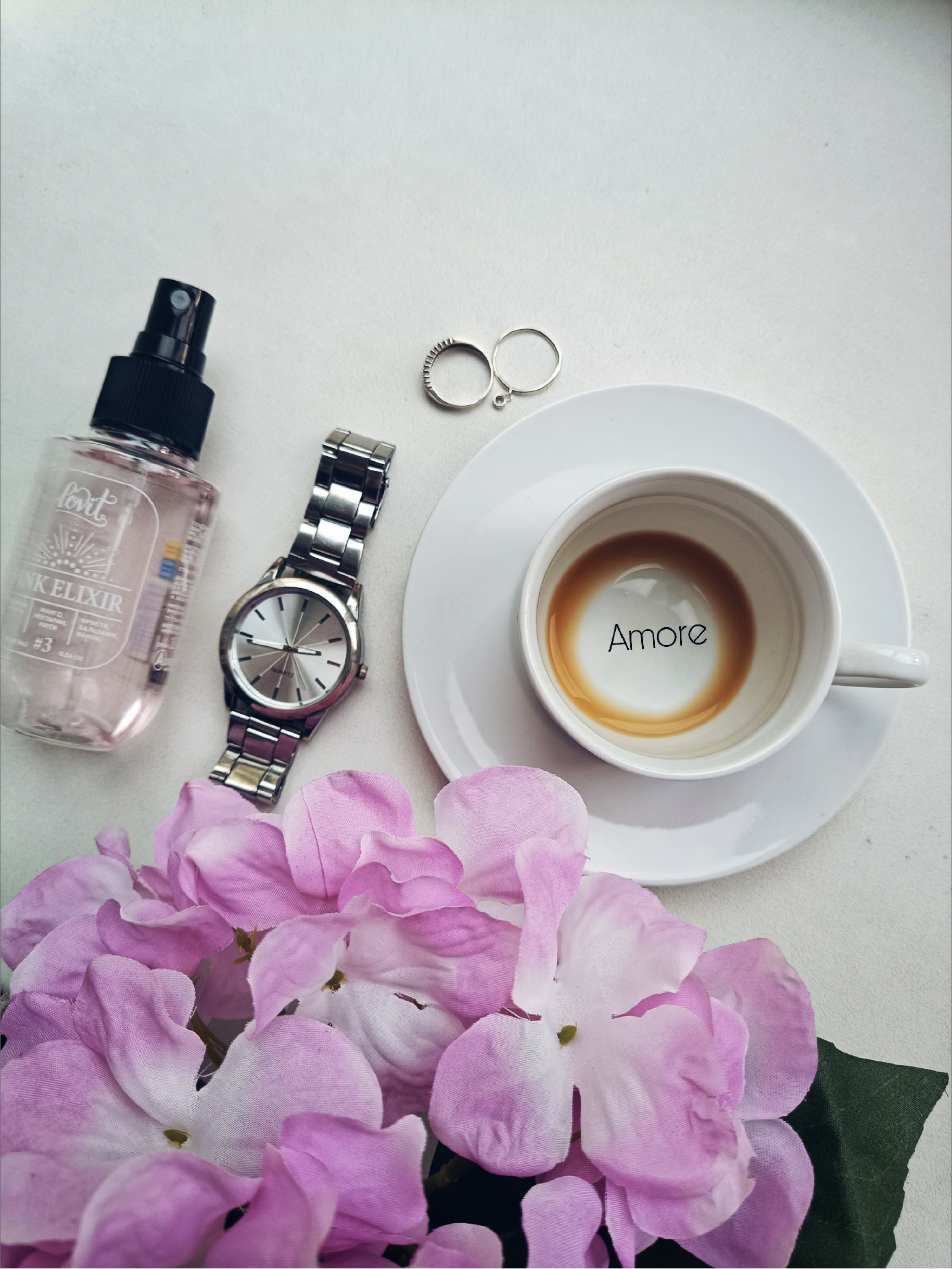 Chic flat lay with coffee, watch, flowers, rings, and perfume for a stylish morning vibe.
