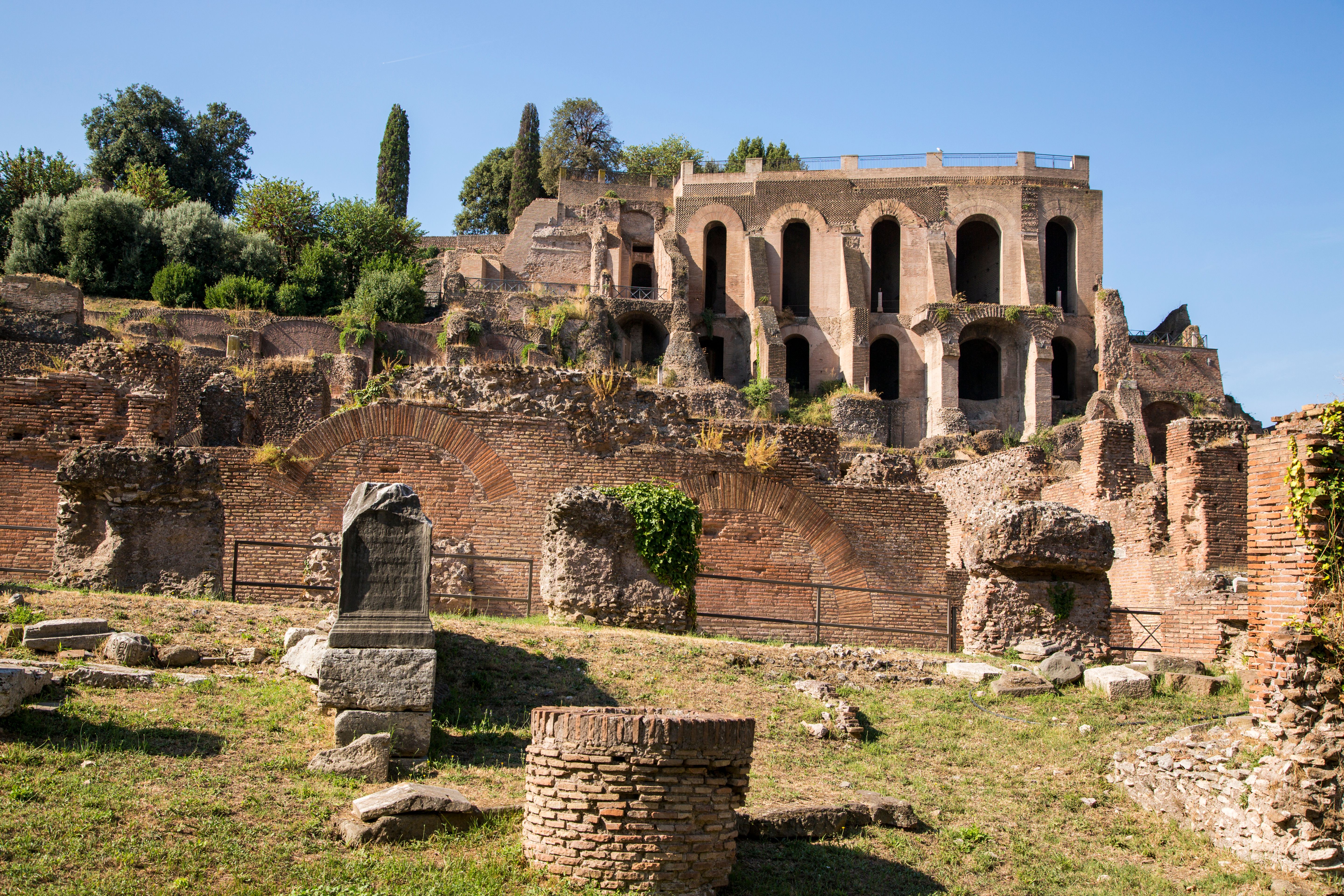 Explore the historic Roman ruins with ancient architecture and vibrant greenery under a clear blue sky.